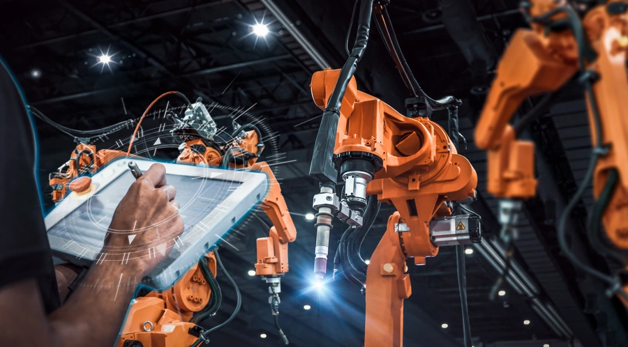 jak wdrożyć sztuczną inteligencję w firmie (pomarańczowe ramiona robotów, a po lewej ręka coś rysująca na tablecie)