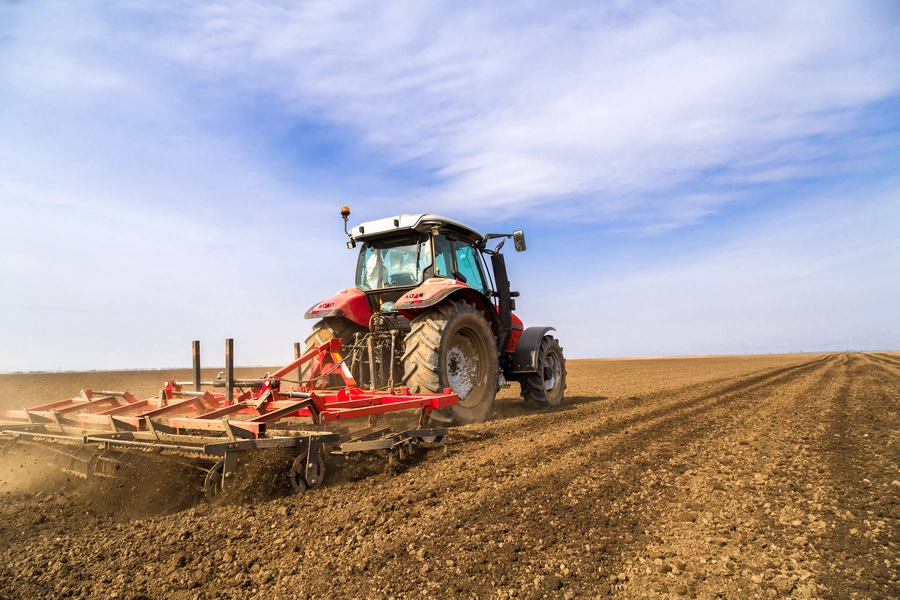 Technology in agriculture (a tractor with its back to us drives through a field with a farm machine attached to the back)