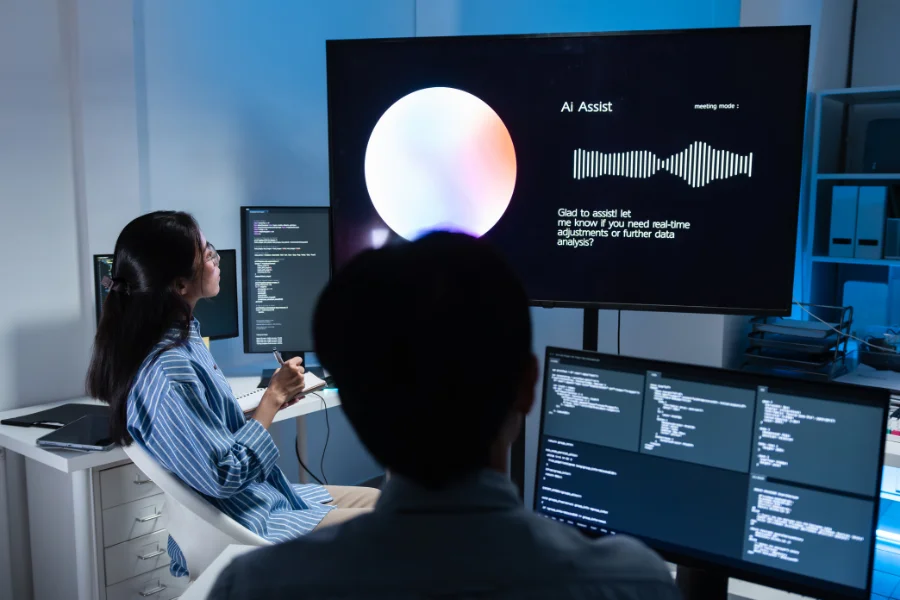 Zwrot z inwestycji w AI - AI jako asystent w operacjach i administracji (dwoje ludzi obserwujących monitor z asystentem AI)